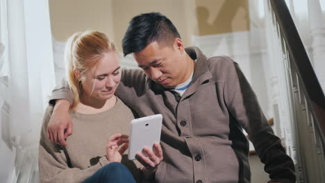 Pareja-Joven-Disfruta-De-Tableta-En-Casa-Sentado-En-Las-Escaleras