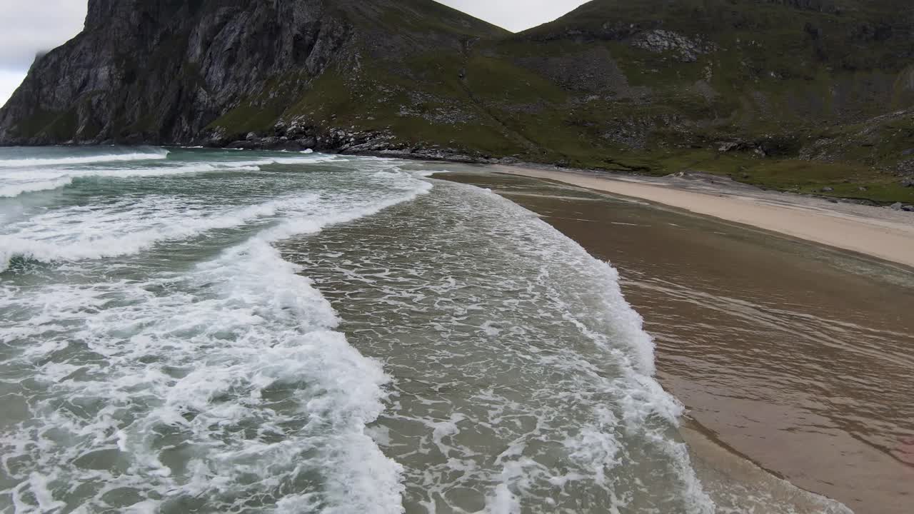 volando sobre el océano y las olas rompiendo en una playa con vistas a las montañas y la playa al pie de la montaña en cámara lenta