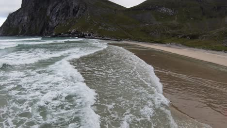 Flying-over-the-ocean-and-the-waves-breaking-at-a-beach-overlooking-the-mountains-and-the-beach-at-the-foot-of-the-mountain-in-slowmotion