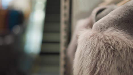 close-up of elegant brown jackets with soft, plush fur collars displayed on hangers, highlighting luxurious textures and modern fashion details, with blurred escalator view in background