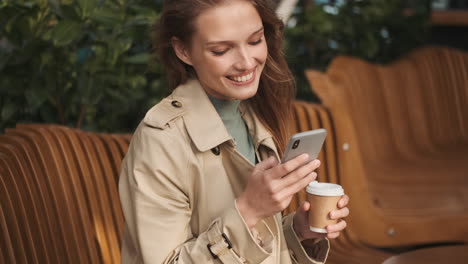 caucasian female student using smartphone and drinking coffee outdoors.