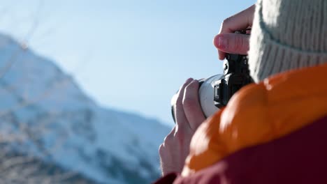 detail of caucasian male hands holding up a camera and photographing winter snowy mountain landscape