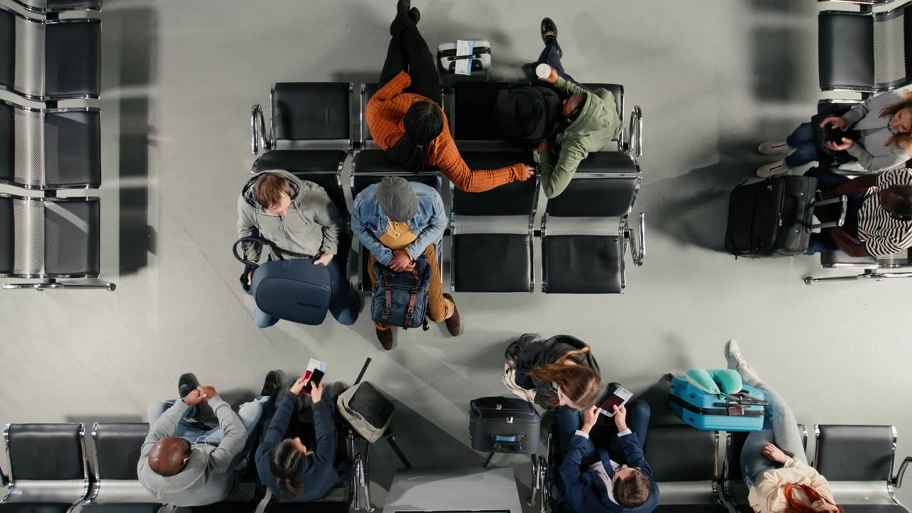 People waiting in airport lounge, checking flight schedule screen
