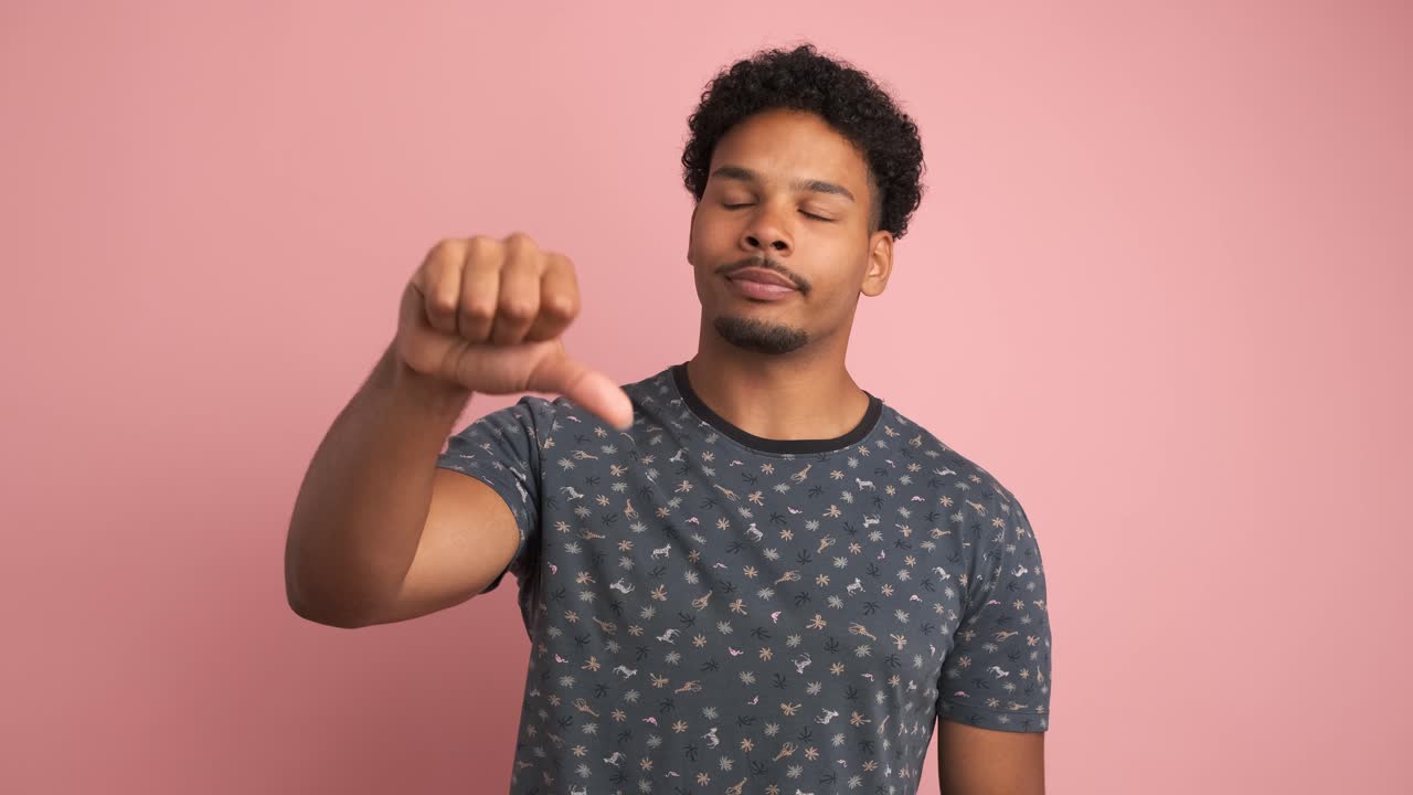 Sad young man showing thumb down in pink studio