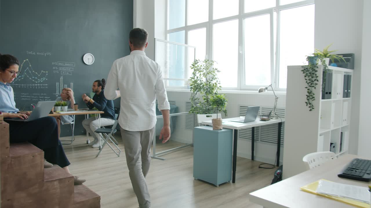 movimiento lento de un joven caminando en una oficina de plan abierto reuniéndose con colegas y luego viendo la presentación de la junta digital