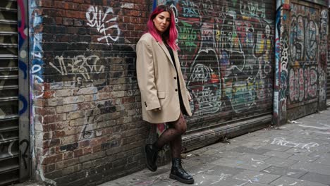 urban style: a fashionable model with pink hair poses confidently against a graffiti-covered wall in a stylish overcoat and trendy boots