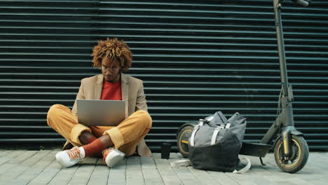 hombre afroamericano bebiendo café y usando una computadora portátil en la calle