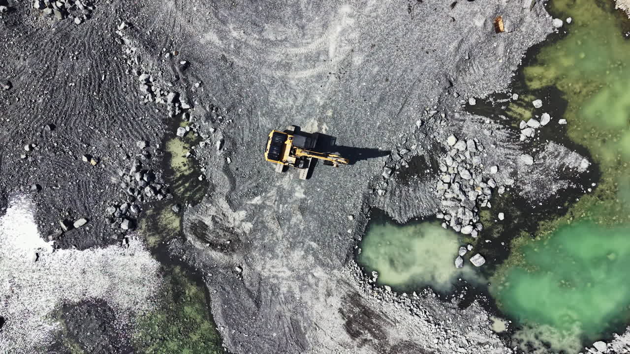 Granite quarry in operation with machinery moving and water pools present at the site during daylight