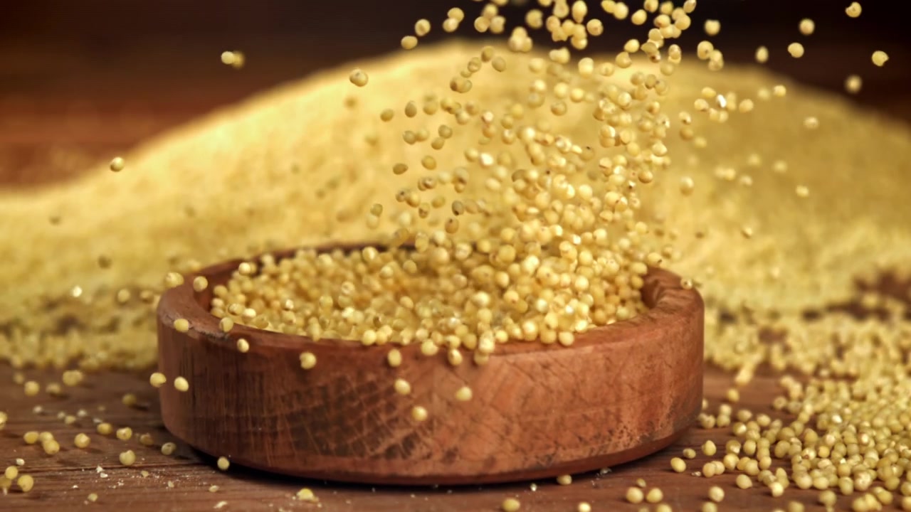 Grano di miglio che si versa in una ciotola di legno al rallentatore.