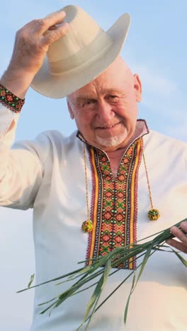Man Making a Happy Gesture with Cowboy Hat Under Sunny Sky at Grassy Event. A man in a cowboy hat and white shirt holds a handful of grass, standing under the sunny sky