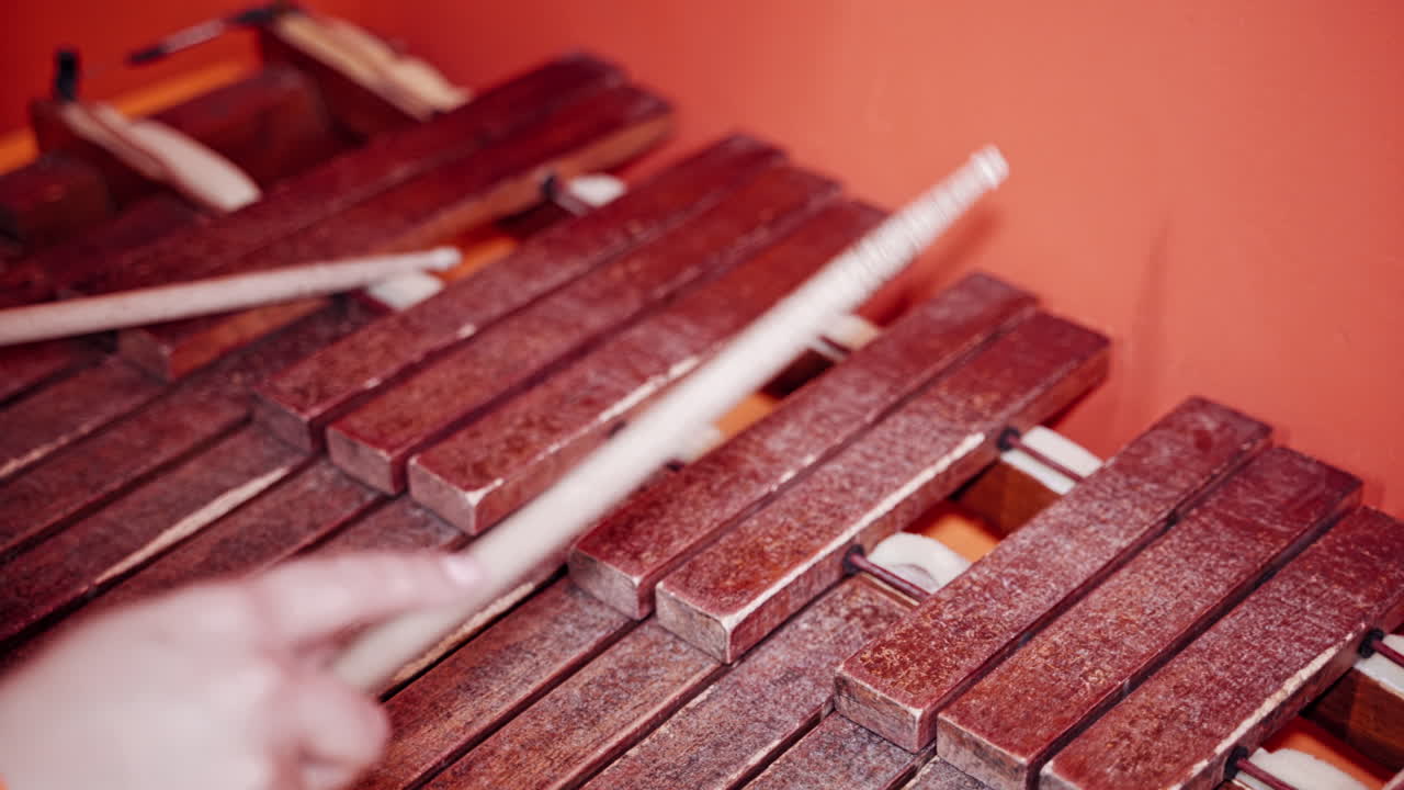 Close-up hands playing the xylophone with sticks on the red background. Old musical instrument. Wooden sticks playing on the brown keys of the xylophone.