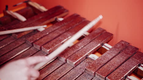 close-up hands playing the xylophone with sticks on the red background. old musical instrument. wooden sticks playing on the brown keys of the xylophone.