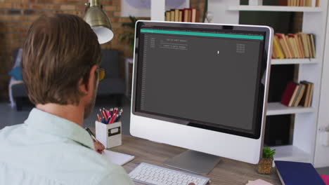 hombre caucásico sentado en un escritorio viendo el procesamiento de datos de codificación en la pantalla de la computadora