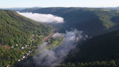 drone pans right over fog drifting above the elbe river and a quiet hillside village near decin, czech republic