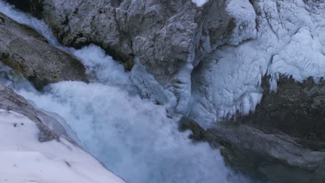 water falling from mountain cliffs between frozen range at winter splashing on rocky slopes