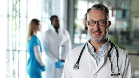 portrait  shotof senior physician wearing a white gown, stethoscope and glasses and looking at camera and smiling in clinic