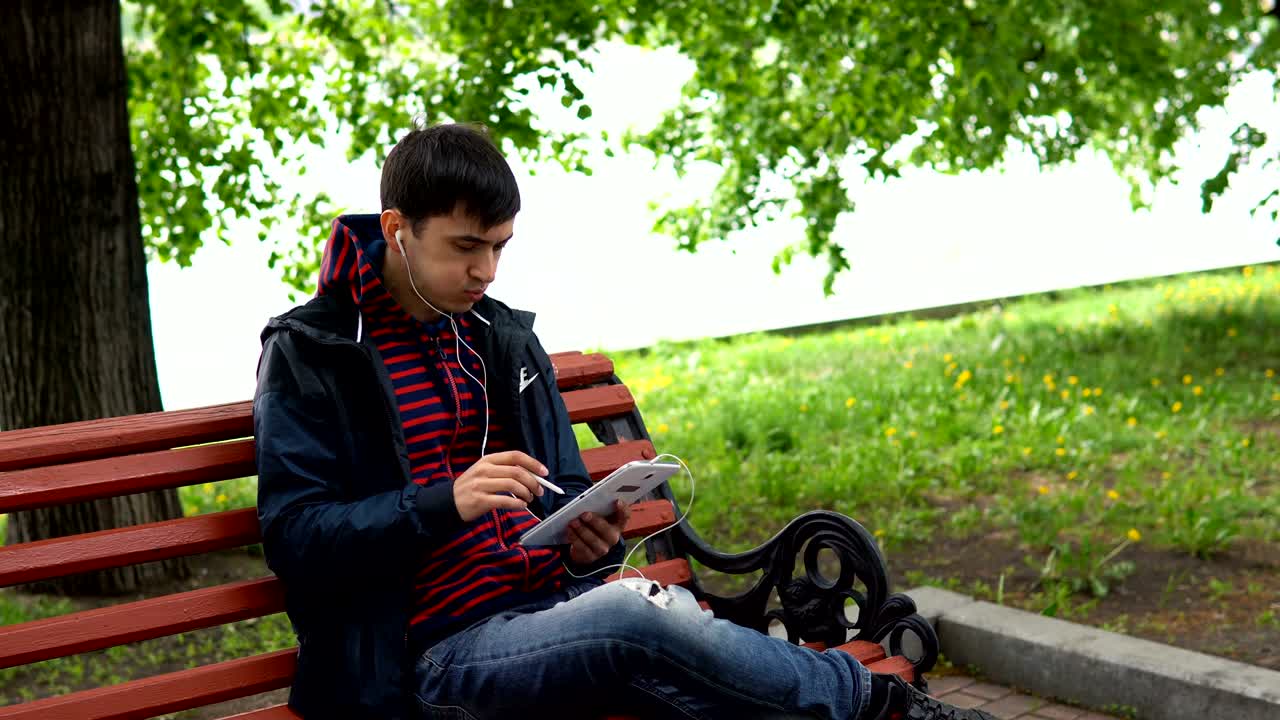 한 남자가 공원에서 음악을 듣고 태블릿을 사용하고 있습니다.