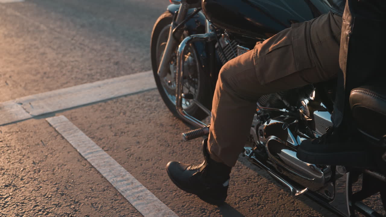 Biker prepares to take off on motorcycle with chrome details shining under warm sunset light, road markings visible on asphalt adding cinematic atmosphere of motion