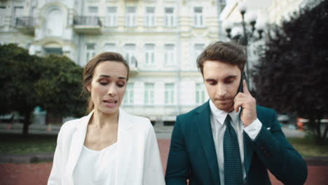 Hombre-De-Negocios-Hablando-De-Teléfono-Móvil-En-El-Paseo-De-La-Ciudad.-Mujer-Caminando-Con-Un-Hombre-Al-Aire-Libre