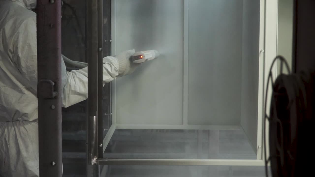 Worker Spray Painting Metal Parts in a Booth