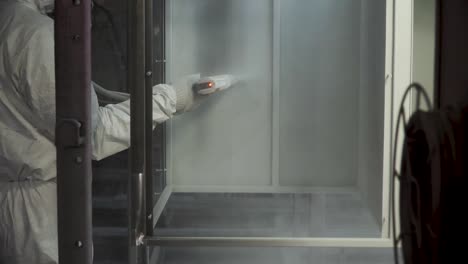 worker spray painting metal parts in a booth