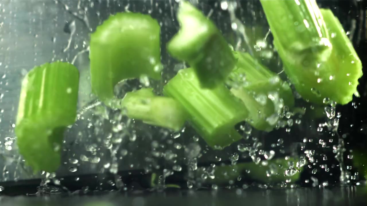 Fresh Green Celery Stalks Splashing with Water and Falling in Slow Motion
