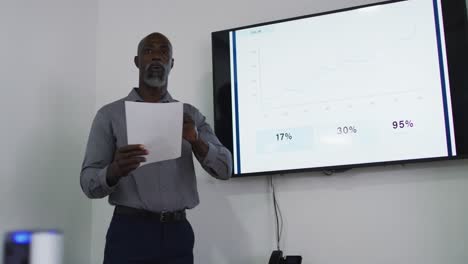 african american businessman talking and pointing at screen, giving presentation in office