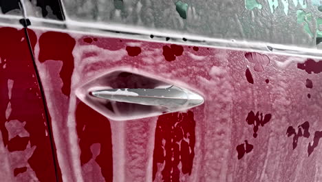 red car exterior covered in foam at wash process carwash, aluminium door handles