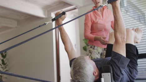 hombre caucásico senior usando reformador en clase de pilates con entrenadora femenina, inalterado, en cámara lenta