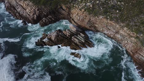 Aerial-Overhead-shot-of-ocean-breaking-and-splashing-on-the-rocky-cliffs