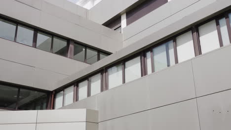 Edificio-De-Hospital-De-Forma-Cuadrada-En-Un-Día-Soleado-Con-Una-Mujer-Que-Trabaja-Limpiando-La-Ventana-Edificio-Moderno