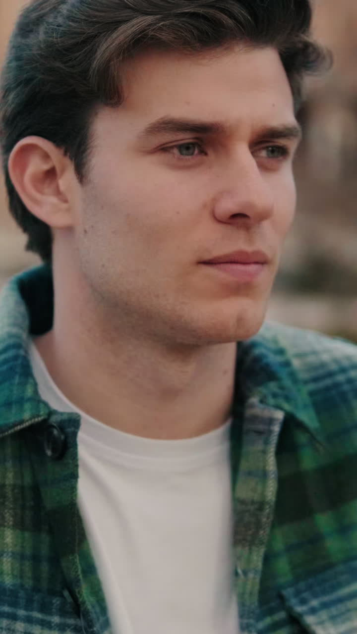 Close-up of young man turning his head and looking at camera with smile on old