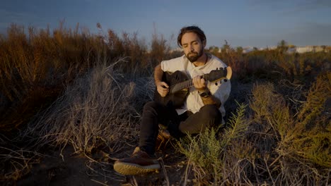 man playing guitar in a field at sunset