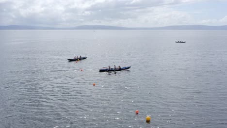 Sideview-tracking-athletes-rowing-with-strength-currach-boats-across-open-ocean