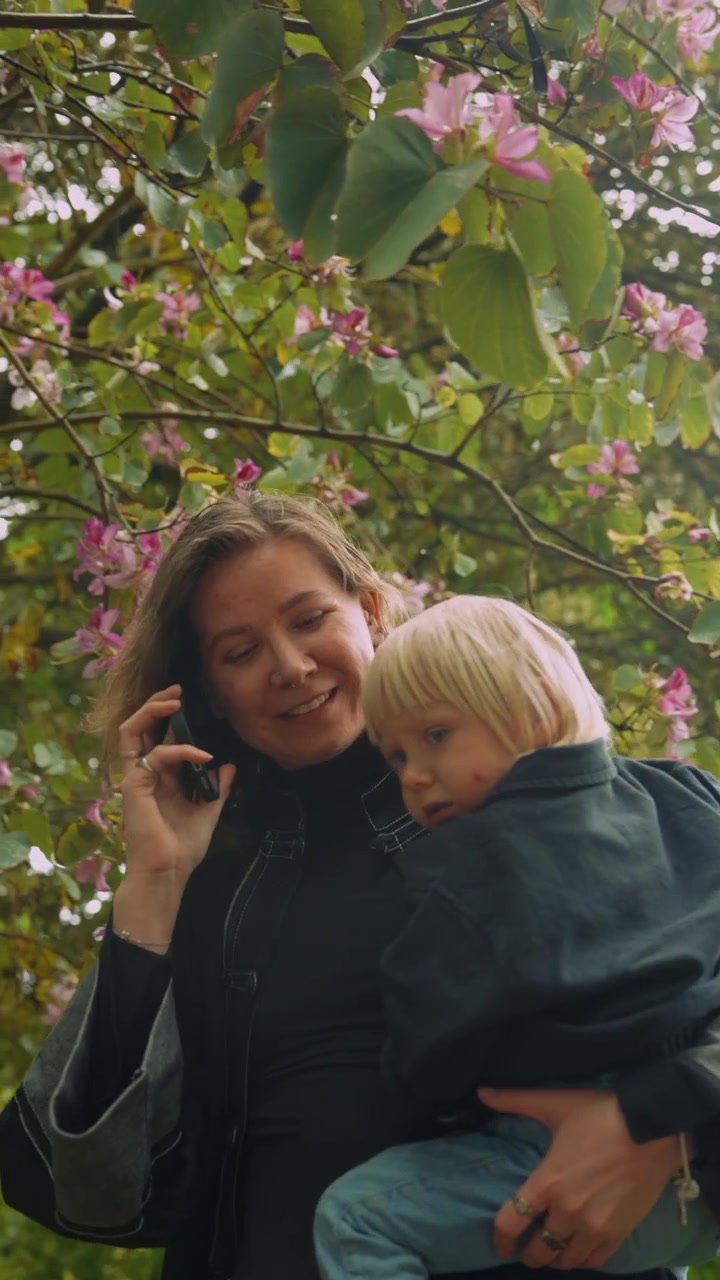 Mutter telefoniert mit Kind unter blühendem Baum