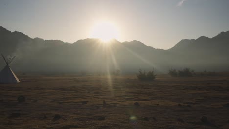 Establisher-pan-of-desert-landscape-with-single-Tepee-tipi-tent-golden-hour-sunshine,-Tipi-in-native-american-reserve-land