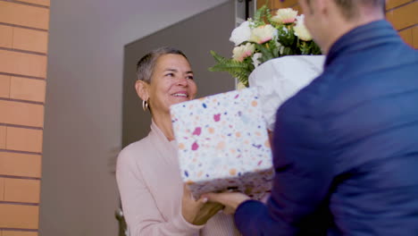 courier delivering flowers and gift box to a surprised woman at her home