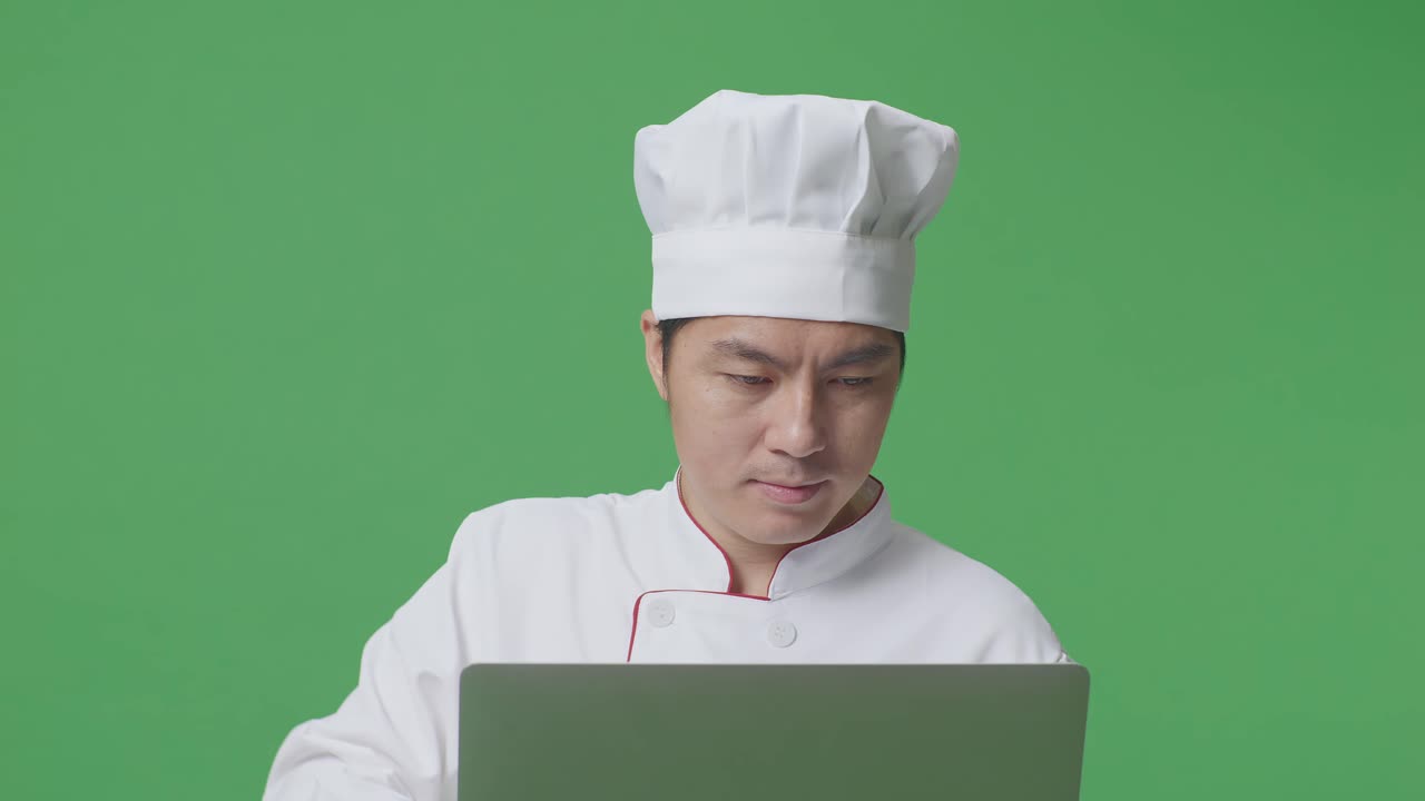 Close Up Of Asian Man Chef Using A Laptop While Standing In The Green Screen Background Studio