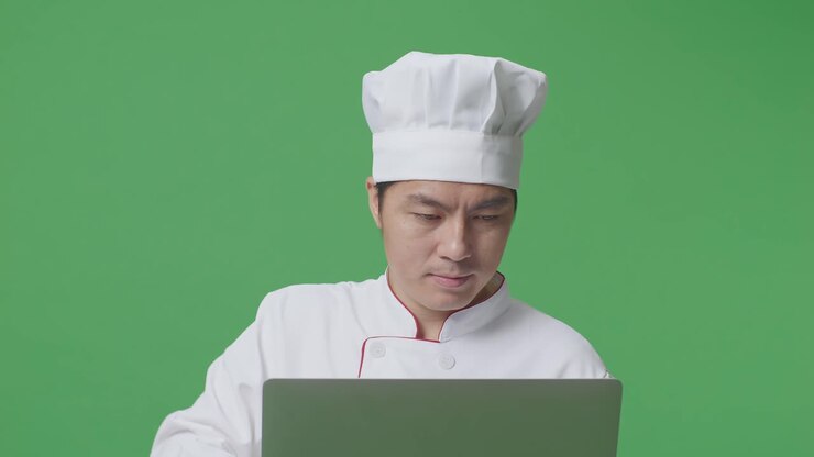 Close Up Of Asian Man Chef Using A Laptop While Standing In The Green Screen Background Studio