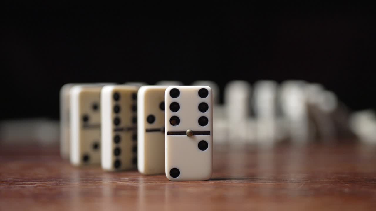 A finger pushes a spiral of white dominos, triggering a slow-motion chain reaction and domino effect in motion