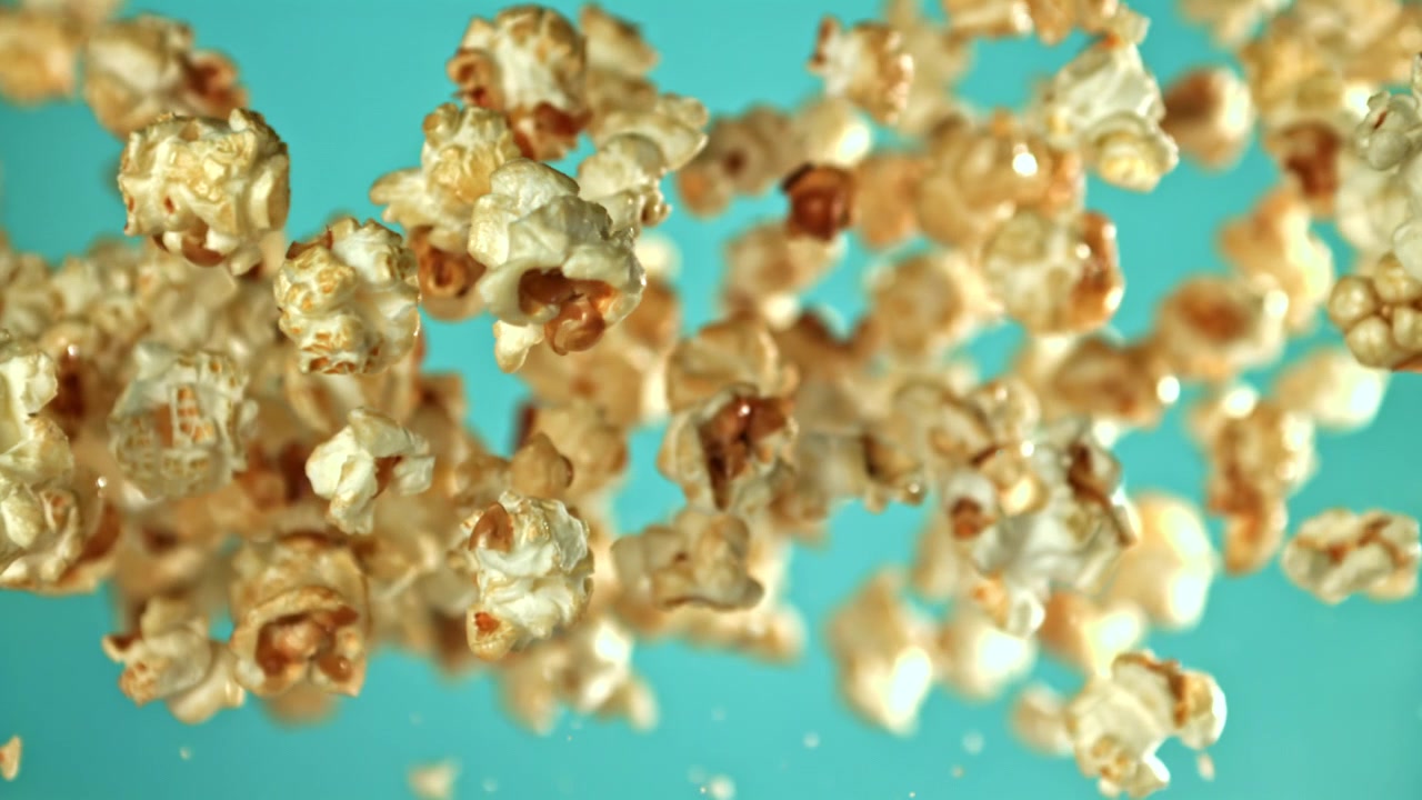 Popcorn deliziosi che cadono al rallentatore su sfondo verde acqua