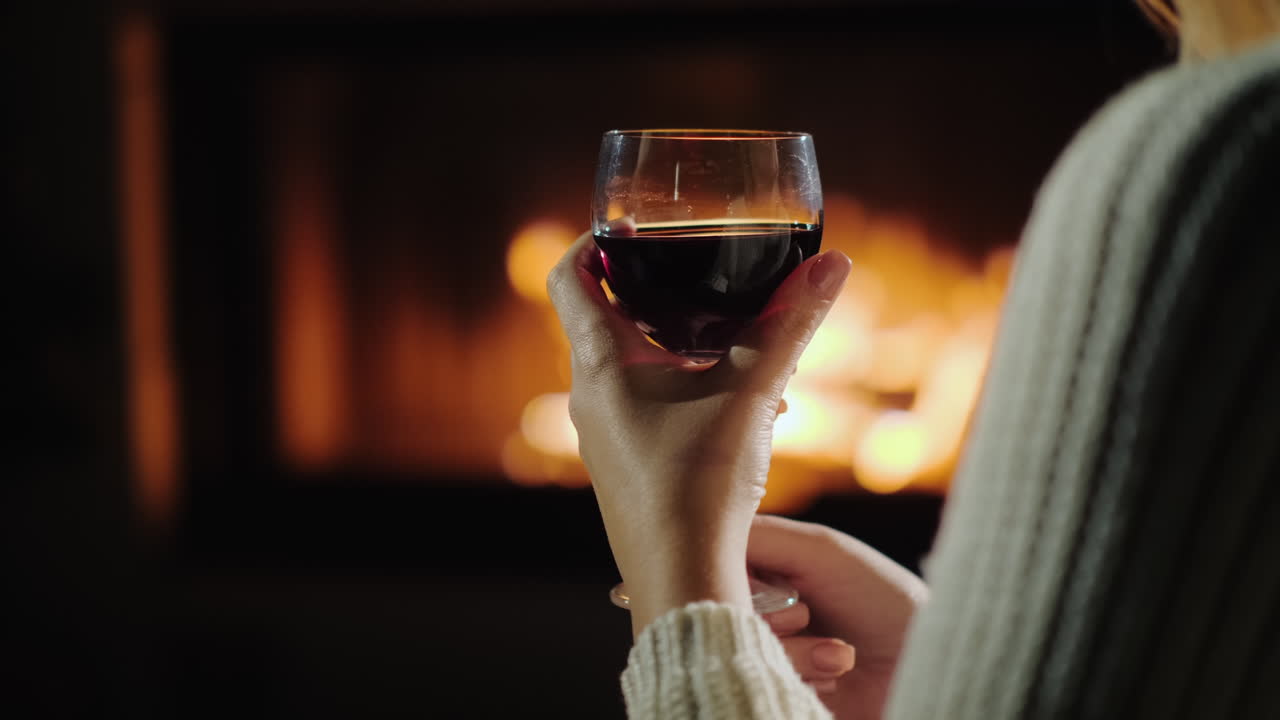 mano femenina con una copa de vino tinto sobre un fondo de llamas en una chimenea