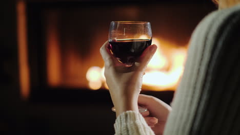 female hand with a glass of red wine on a background of flame in a fireplace