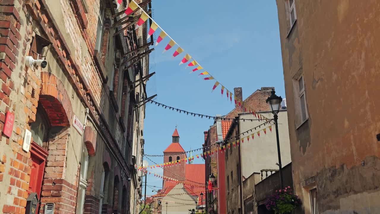 Cinematic old town in Grudziadz with flags hanging above narrow street view