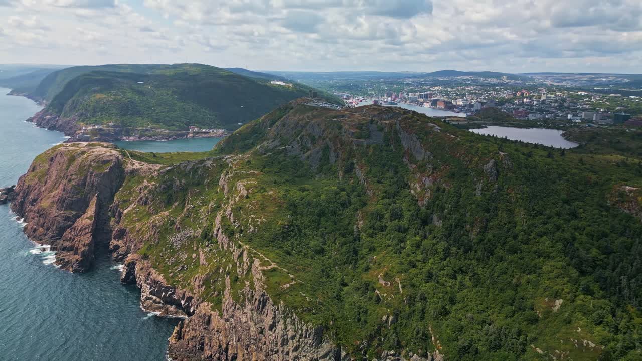 A drone sweeps along Signal Hill's lush green cliffs, revealing dramatic drops to the Atlantic Ocean and rocky shoreline under an expansive sky