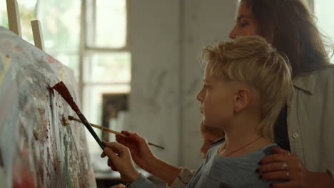 focused boy drawing with teacher indoors. mother and son painting in studio.