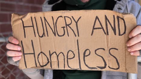 close up shot of homeless man shifting and holding sign saying, "hungry and homeless"