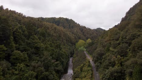 Drone-following-a-jungle-river-next-to-a-narrow-road-that-goes-through-a-mountain-valley