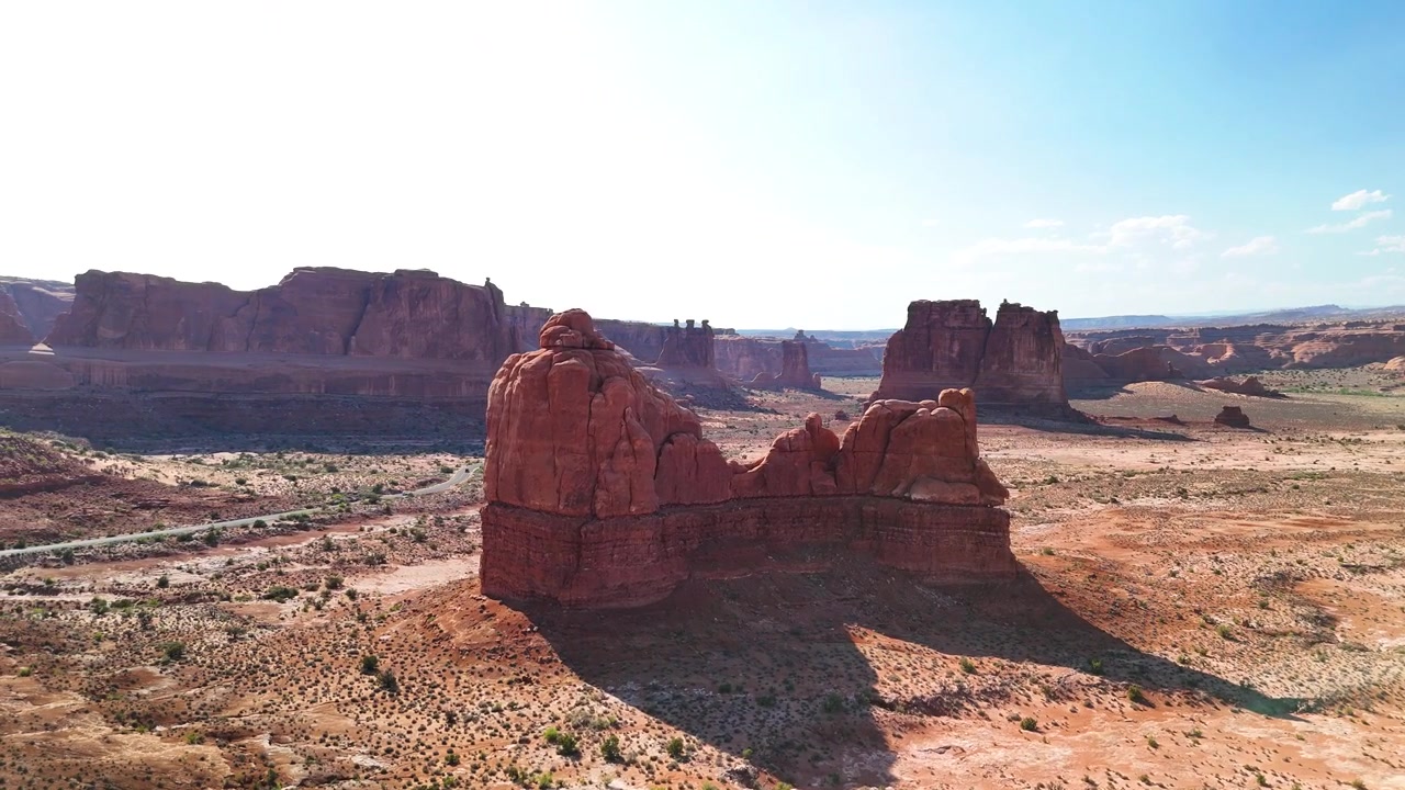 Stunning stock footage of Arches National Park USA during a bright afternoon. The brilliant sunlight illuminates the majestic red rock sandstone structures and desert landscape under a clear blue sky.