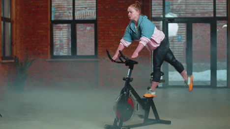 healthy caucasian woman exercising workout on stationary cycling machine bike in gym, slow motion